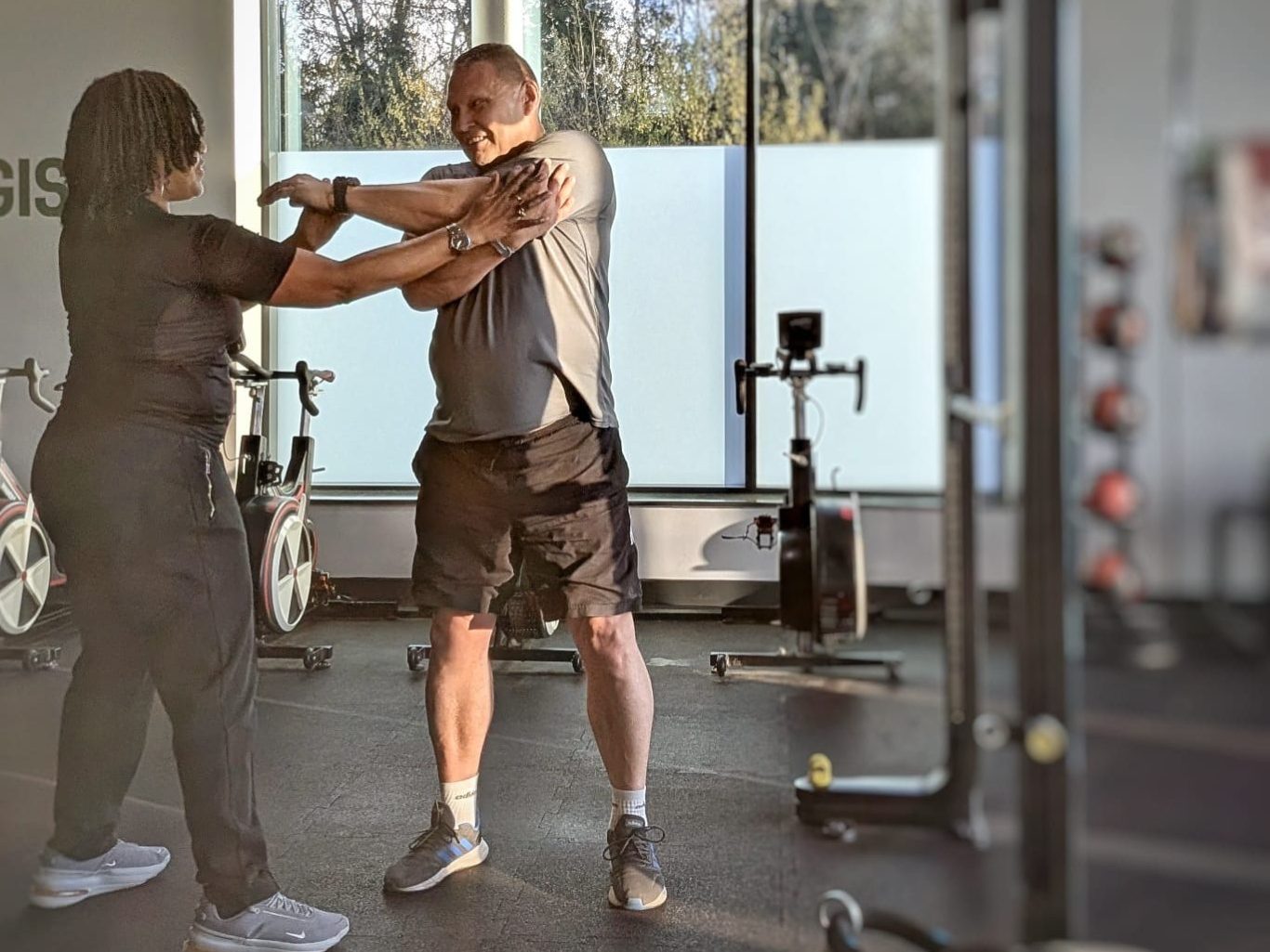 "One-to-One Personal Training Session with Sophia" "Sophia assisting a male client with an arm stretch in the gym."
